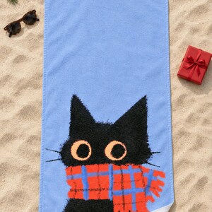 Plaid scarf black cat beach towel laid flat on sand with sunglasses, one corner folded to show the white back.