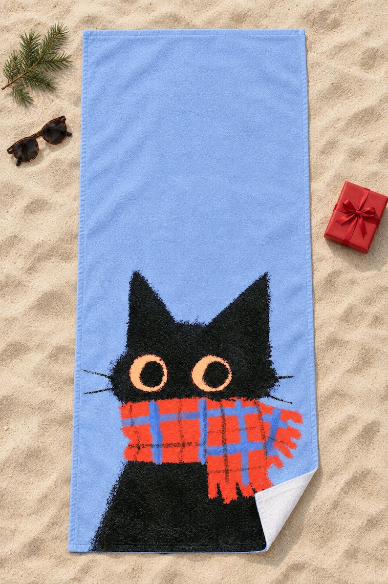 Plaid scarf black cat beach towel laid flat on sand with sunglasses, one corner folded to show the white back.