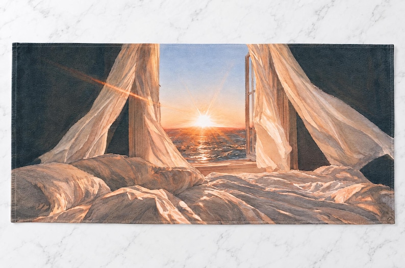 May include: A rectangular towel featuring a printed scene of a sunrise over the ocean viewed from an open window. White curtains blow inward over a rumpled bed with white bedding. The dark interior contrasts with the bright orange sun.