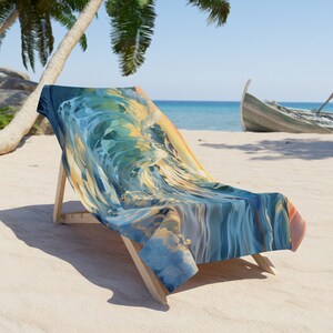 Ocean wave beach towel draped over a wooden beach chair on white sand, the print a swirling blue and teal wave with golden sunset light, palm trees and a turquoise sea behind.