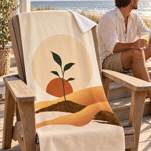 Boho sun seedling beach towel draped over a wooden Adirondack chair on a seaside deck, a top corner folded back to the white terry back; a man in sunglasses and a white linen shirt sits nearby holding a drink.