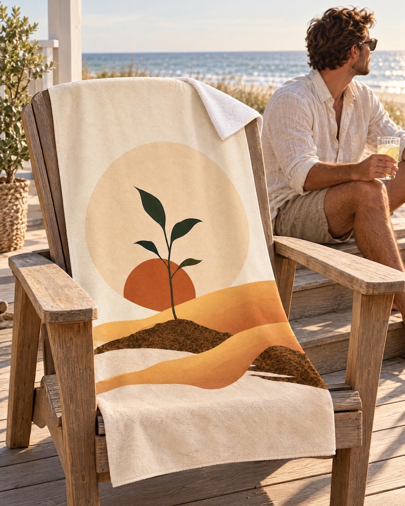 Boho sun seedling beach towel draped over a wooden Adirondack chair on a seaside deck, a top corner folded back to the white terry back; a man in sunglasses and a white linen shirt sits nearby holding a drink.