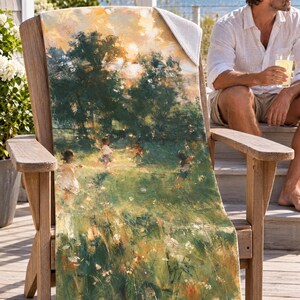 Impressionist garden beach towel draped over a wooden Adirondack chair on a seaside deck, a top corner folded back to the white terry back; a man in sunglasses and a white linen shirt sits nearby holding a drink.