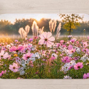 Peut inclure: Un tapis de bain rectangulaire pr&eacute;sentant une impression photographique haute r&eacute;solution d'une prairie fleurie de cosmos roses et blancs. La sc&egrave;ne est &eacute;clair&eacute;e par un lever de soleil dor&eacute;, avec des herbes hautes et des arbres en arri&egrave;re-plan.