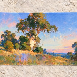 May include: A rectangular beach towel featuring a printed landscape painting of a large tree on a grassy hillside under a blue and pink sky. The artwork displays visible brushstrokes in shades of green, yellow, orange, and blue across the fabric.