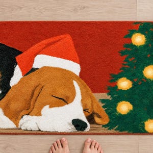 Sleeping beagle Santa hat bath mat seen from above on a light wood floor, with rolled white towels, a candle, pine sprigs and bare feet at the bottom edge.