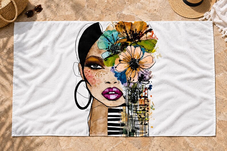 May include: A white rectangular beach towel featuring a stylized illustration of a face with dark hair, large hoop earrings, and bright pink lips. The design incorporates vibrant watercolor-style flowers in orange, blue, and green, alongside black and white stripes.