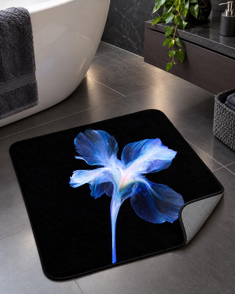 May include: A square bath mat with a solid black background featuring a large, vibrant blue iris flower graphic in the centre. The flower petals display shades of deep blue, light blue, and white, with a soft, glowing light effect at the base.