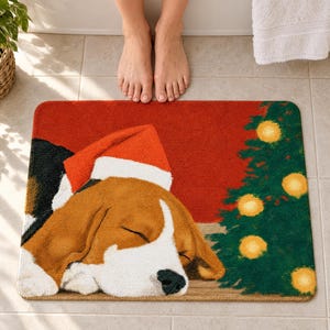 Bath mat with a painted beagle asleep in a red-and-white Santa hat beside a small Christmas tree with glowing lights on a red wall, on a tiled floor by a tub with bare feet beside it.