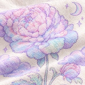 May include: A white textured fabric featuring an embroidered design of a large blooming flower in shades of pastel pink, purple, and blue. The floral motif is surrounded by small embroidered stars, a crescent moon, and fluffy cloud shapes.