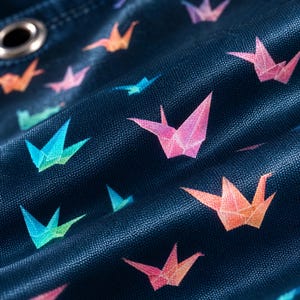 Pu&ograve; includere: Un tessuto blu scuro con un motivo ripetuto di gru origami colorate nelle tonalit&agrave; del rosa, arancione e turchese. Il materiale presenta una trama visibile e include un singolo occhiello metallico nell'angolo in alto a sinistra dell'immagine.