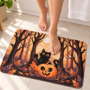 Black cat and jack-o'-lantern bath mat with ghosts, a full moon and bare autumn trees on a tiled bathroom floor in front of a white bathtub with a towel on its edge; one bare foot steps onto the mat.