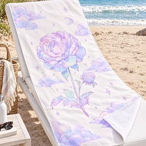 May include: A white rectangular beach towel featuring a large, central illustration of a blooming peony flower in shades of pastel purple, pink, and blue, surrounded by soft clouds, small stars, and a crescent moon graphic.