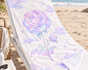 May include: A white rectangular beach towel featuring a large, central illustration of a blooming peony flower in shades of pastel purple, pink, and blue, surrounded by soft clouds, small stars, and a crescent moon graphic.