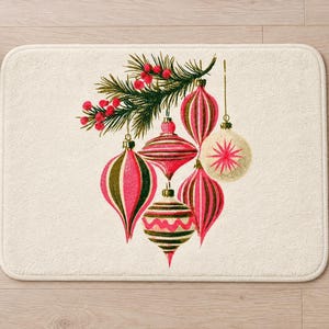Overhead view of the whole retro ornament bath mat on a light wood floor, with a lit candle and a berry pine sprig on one side and rolled white towels on the other.