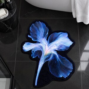 May include: A shaped bathroom rug featuring a large, detailed iris flower design. The petals transition from deep navy blue at the edges to vibrant shades of electric blue, violet, and a soft white centre, all set against a solid black background.