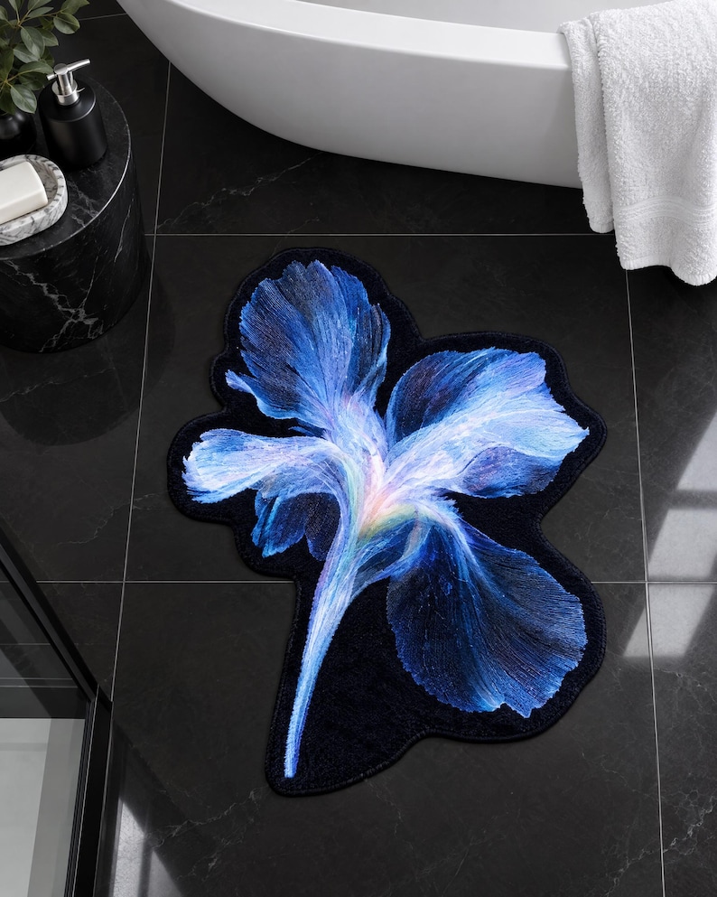 May include: A shaped bathroom rug featuring a large, detailed iris flower design. The petals transition from deep navy blue at the edges to vibrant shades of electric blue, violet, and a soft white centre, all set against a solid black background.