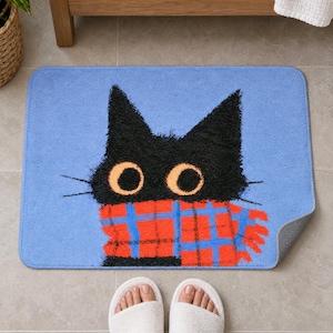 Plaid scarf black cat bath mat in front of a wood vanity, one corner turned up to show the gray anti-slip back, with white slippers below.
