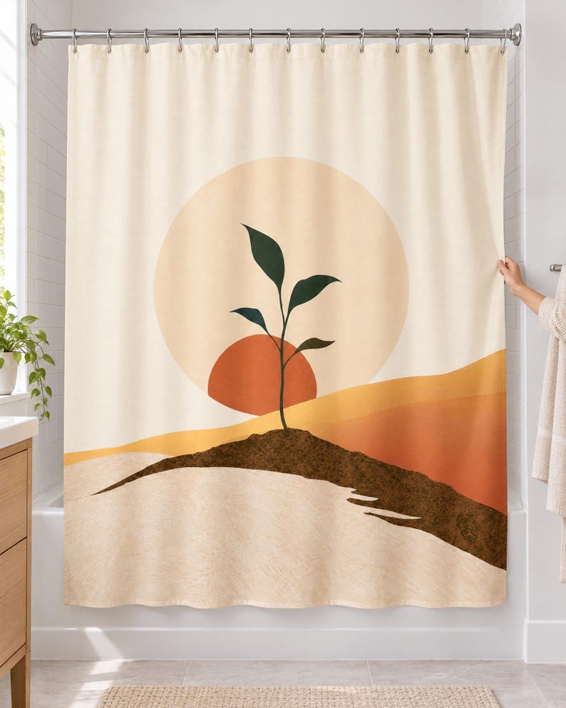 Boho seedling sun shower curtain over a bathtub in a white-tiled bathroom: a dark green sprout on a brown soil ridge before a terracotta half sun and pale circle, with ochre and rust hills on cream; a hand pulls back the right edge.