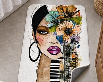 May include: A rectangular bath mat featuring a stylized illustration of a person's face with dark hair, bright purple lips, and large hoop earrings. The design includes colorful watercolor-style flowers and black and white striped patterns.