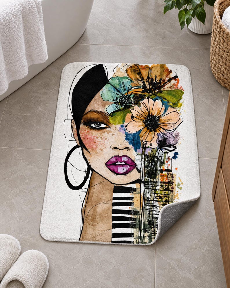 May include: A rectangular bath mat featuring a stylized illustration of a person's face with dark hair, bright purple lips, and large hoop earrings. The design includes colorful watercolor-style flowers and black and white striped patterns.