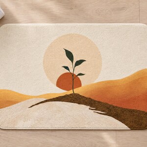 Overhead view of the whole boho sun sprout bath mat on a light wood floor, with rolled white towels, a lit candle and a small potted plant in a terracotta pot beside it.