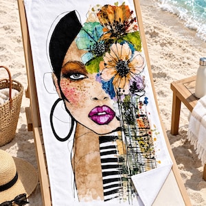 May include: A white rectangular beach towel featuring a stylized watercolor illustration of a face adorned with vibrant orange, yellow, and blue flowers. The design includes bold black line work, bright pink lips, and a black and white striped pattern.