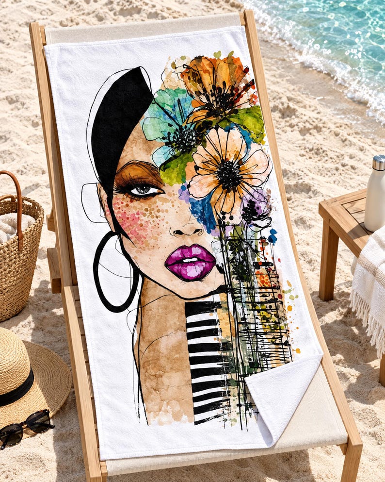 May include: A white rectangular beach towel featuring a stylized watercolor illustration of a face adorned with vibrant orange, yellow, and blue flowers. The design includes bold black line work, bright pink lips, and a black and white striped pattern.