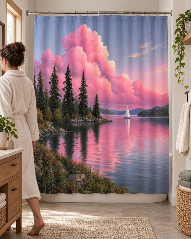 Wider view of a bright bathroom with the pine lake sailboat shower curtain closed across the tub and a woman in a white robe standing barefoot in front of it, partly hiding the pines, beside a wooden vanity.