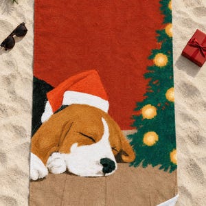 Sleeping beagle Santa hat beach towel laid flat on sand with sunglasses, a pine sprig and a small red gift box, one corner folded to show the white back.