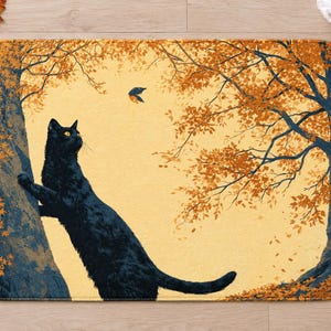 Overhead view of the whole climbing cat autumn bath mat on a light wood floor, with a lit candle, rolled white towels and fallen maple leaves around it.