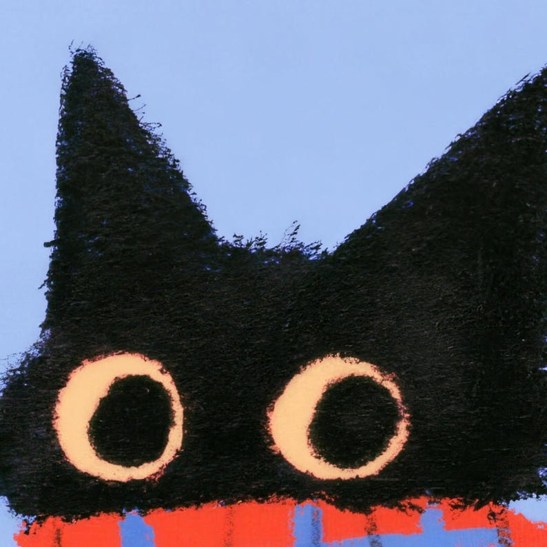 Close-up of the beach towel's print: the black cat's pointed ears and two round cream-ringed eyes above the top of the red plaid scarf on periwinkle blue.