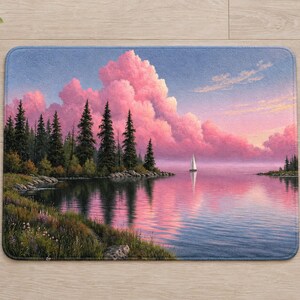 Overhead view of the whole pink cloud lake bath mat on a light wood floor, with rolled white towels, a potted plant, a lit candle and a pine cone around it.