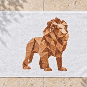 May include: A white rectangular towel featuring a centered geometric lion graphic. The lion is composed of various shades of brown and tan triangular shapes, creating a faceted, low-poly appearance against the plain white fabric background.