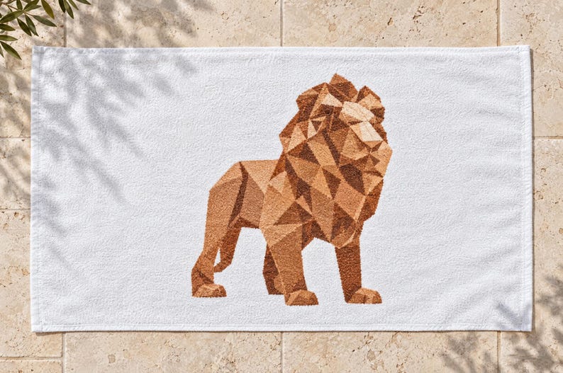 May include: A white rectangular towel featuring a centered geometric lion graphic. The lion is composed of various shades of brown and tan triangular shapes, creating a faceted, low-poly appearance against the plain white fabric background.