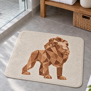May include: A rectangular bath mat in a light beige colour featuring a geometric, low-poly style lion illustration in shades of brown. The lion is depicted in profile, standing on all fours, with a textured surface and rounded corners.