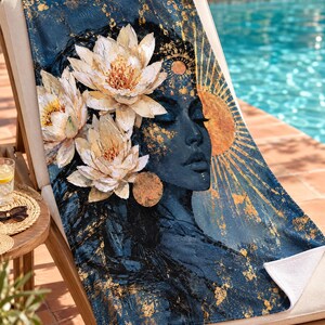 K&ouml;nnte beinhalten: Ein rechteckiges Strandtuch mit dunkelblauem Hintergrund und goldenen Spritzern. Das Design zeigt das Profil einer Person mit geschlossenen Augen, verziert mit drei gro&szlig;en wei&szlig;en Lotusbl&uuml;ten und einer strahlenden goldenen Sonne.