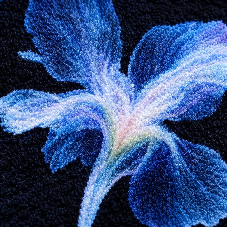 以下が含まれることがあります： 質感のある黒い生地に、大きなアイリスの花の刺繍が施されています。花びらは濃い青、水色、白のグラデーションになっており、中心部には淡い黄色とラベンダー色の繊細な色合いが加わり、詳細な花柄のモチーフを作り出しています。