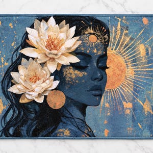 May include: A rectangular bath mat featuring a dark blue illustration of a person in profile with closed eyes. Two large white lotus flowers are tucked into dark hair. A golden sun with radiating beams and gold paint splatters decorate the scene.