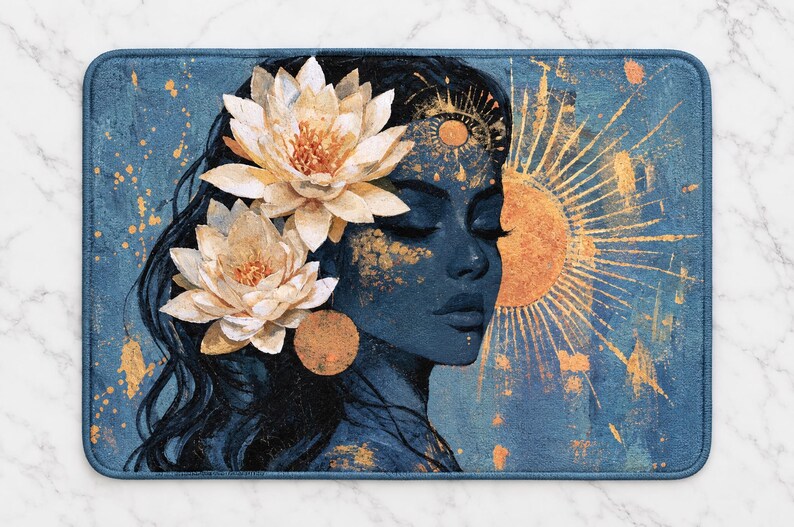 May include: A rectangular bath mat featuring a dark blue illustration of a person in profile with closed eyes. Two large white lotus flowers are tucked into dark hair. A golden sun with radiating beams and gold paint splatters decorate the scene.