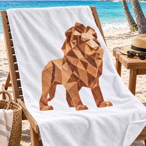 May include: A white beach towel featuring a large, geometric lion graphic composed of various shades of brown and tan triangles. The lion is depicted in a standing profile view, centered on the soft, textured fabric of the rectangular towel.