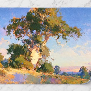 May include: A rectangular bath mat featuring an impressionistic landscape painting of a large, textured tree with green foliage set against a bright blue sky. The foreground shows a grassy hillside with warm yellow, orange, and purple tones.