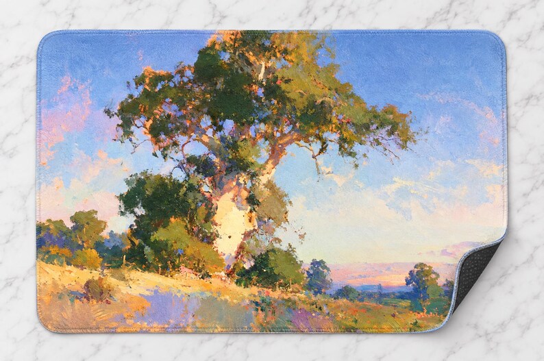 May include: A rectangular bath mat featuring an impressionistic landscape painting of a large, textured tree with green foliage set against a bright blue sky. The foreground shows a grassy hillside with warm yellow, orange, and purple tones.