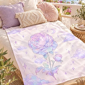 May include: A rectangular throw blanket featuring a large, central pastel-colored peony flower illustration. The design includes soft purple and blue clouds, small four-pointed stars, and a crescent moon against a light, off-white background.