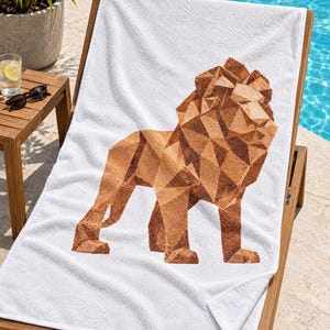 May include: A white rectangular beach towel featuring a large, centered graphic of a lion rendered in a geometric, low-poly style. The lion figure is composed of various shades of brown and tan, creating a faceted, angular appearance on the fabric.