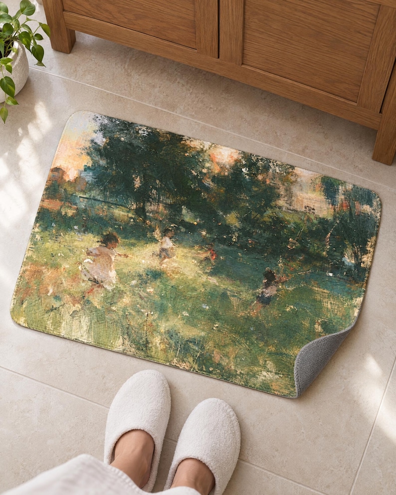 Painterly garden bath mat with children running through a meadow on a tiled floor by a wooden vanity; feet in white slippers rest on the tile in front and one corner flips up to show the gray anti-slip back.