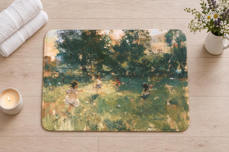 Overhead view of the whole impressionist garden bath mat on a light wood floor, with rolled white towels, a lit candle and a small white vase of daisies and purple wildflowers beside it.