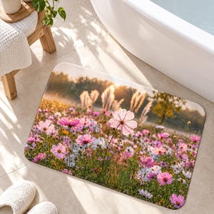 Peut inclure: Un tapis de bain rectangulaire orn&eacute; d'une impression photographique repr&eacute;sentant une prairie ensoleill&eacute;e remplie de fleurs de cosmos roses et blanches, d'herbes hautes et d'une lumi&egrave;re dor&eacute;e, aux coins arrondis.
