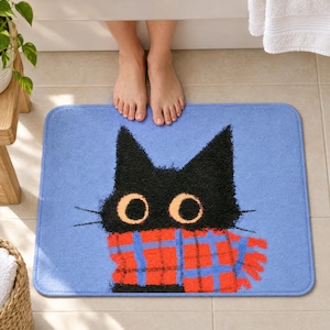 Bath mat with a fluffy black cat with big round eyes in a red plaid scarf on periwinkle blue, on a tiled bathroom floor by a tub with bare feet resting on it.