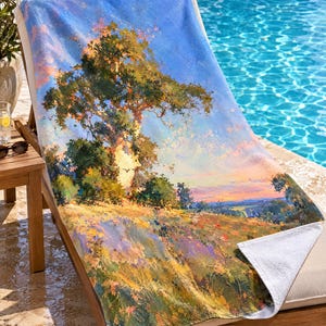 May include: A rectangular beach towel featuring an impressionistic landscape painting of a large tree on a grassy hill under a blue sky. The artwork displays vibrant shades of green, yellow, orange, and blue, with a white underside visible at the corner.